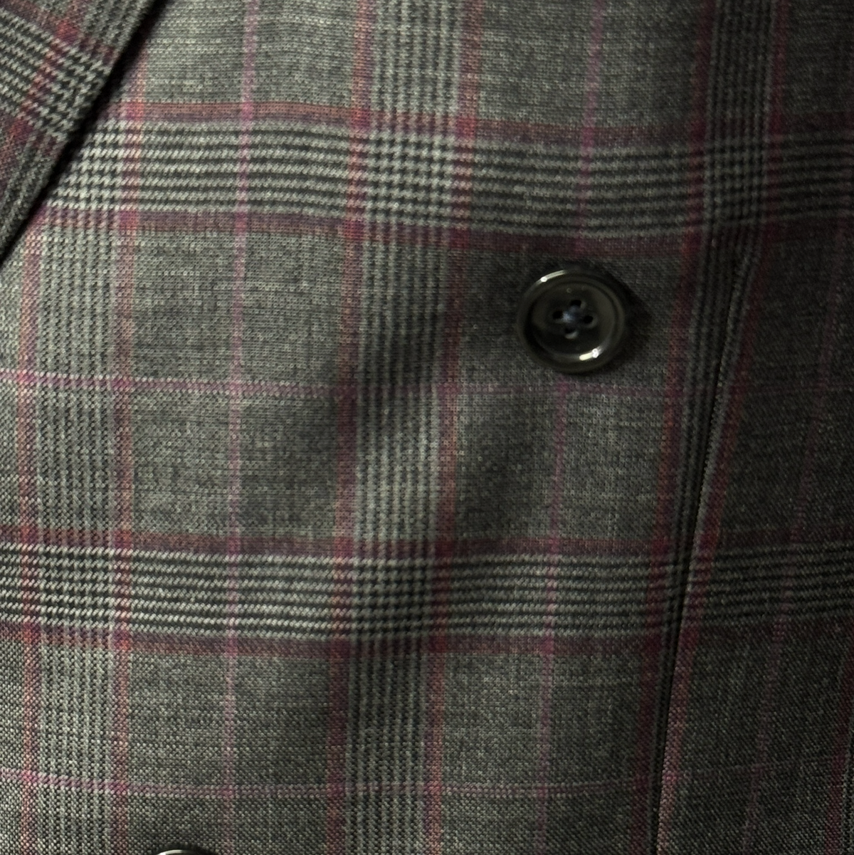 A man in a gray Tiglio Luxe PISTOIA Modern Fit Double Breasted Suit TL9172 by Tiglio stands on a wooden floor in a formal setting, surrounded by clothing racks and suits. His Italian-made Super 150’s wool suit showcases timeless craftsmanship and refined style.