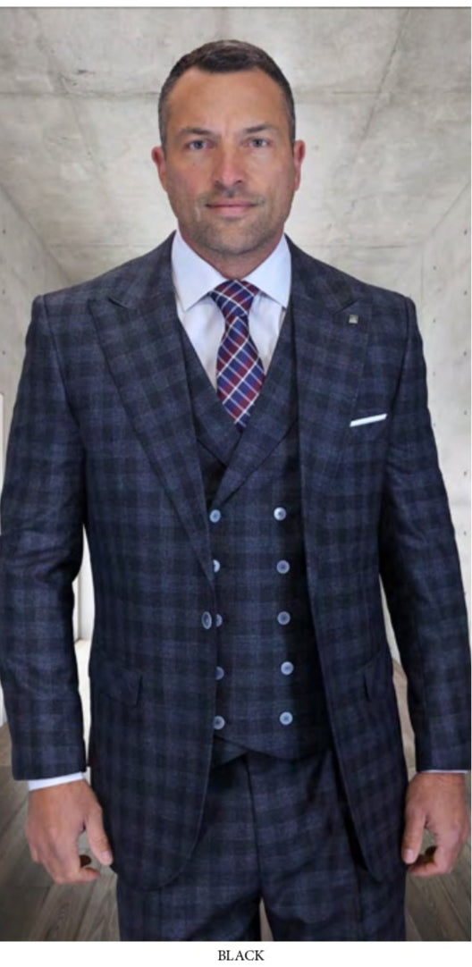 A man in STATEMENT CLOTHING | BALANCIGA-BLACK by Statement Clothing—a dark plaid three-piece suit with wide-leg pants—wears a white shirt and striped tie, standing in a modern room with concrete walls and wood floor.