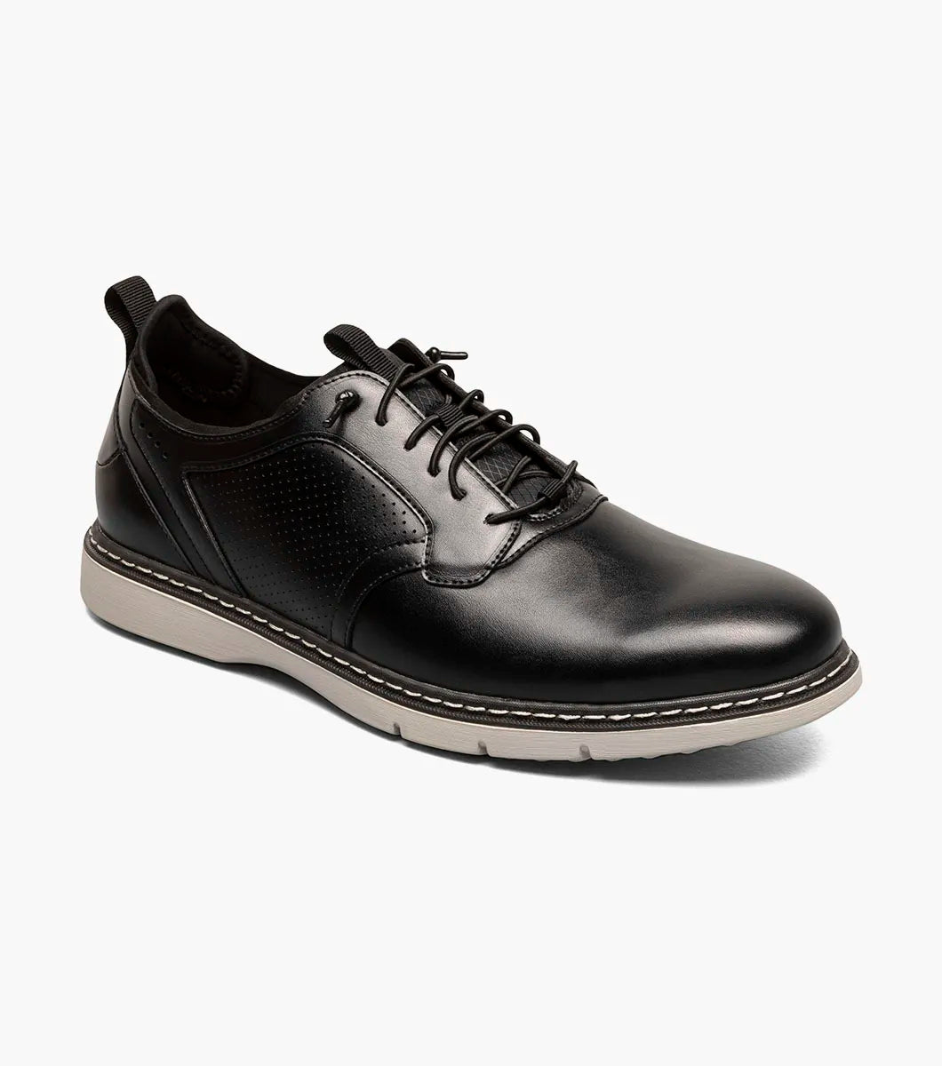 The Stacy Adams Score Plain Toe Elastic Lace Up in black features a leather upper with light gray rubber sole, white stitching, and perforated detailing on the side. Seen from a slight angle, this STACY ADAMS shoe blends refined business-casual style with everyday comfort.