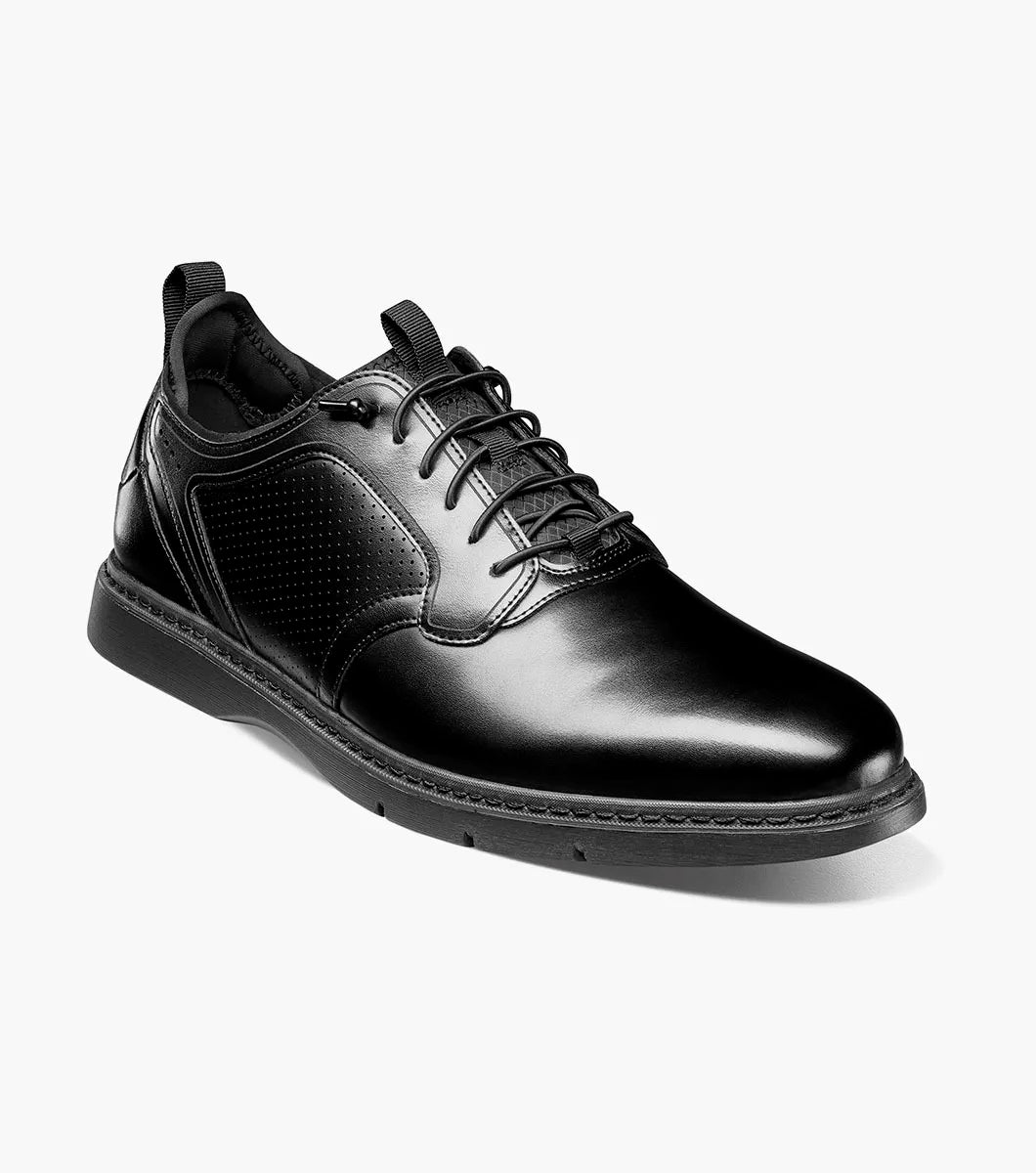 The Stacy Adams Score Plain Toe Elastic Lace Up in Black Smooth (Style 21538-005) is a black leather dress shoe featuring elastic laces, a low heel, a textured sole, and subtle perforated detailing on the side. It includes the RedZone footbed for enhanced comfort and is presented in a side profile against a white background.