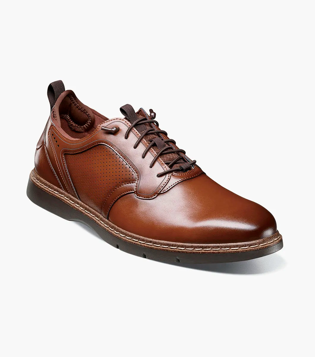 A single Stacy Adams Score Plain Toe Elastic Lace Up dress shoe in Cognac Smooth leather, featuring a textured side panel and a comfortable RedZone footbed, is shown at an angle on a white background.