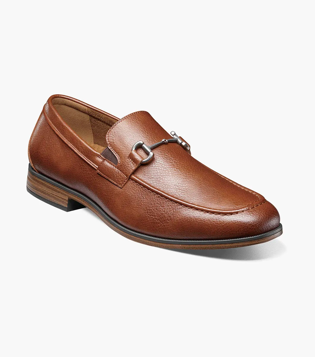 The STACY ADAMS Richmont Moc Toe Bit Slip On in Cognac Tumbled (21567-222) is a brown leather loafer with a metal bit, moc toe slip-on design, low wooden heel, and detailed toe stitching, shown on a white background.