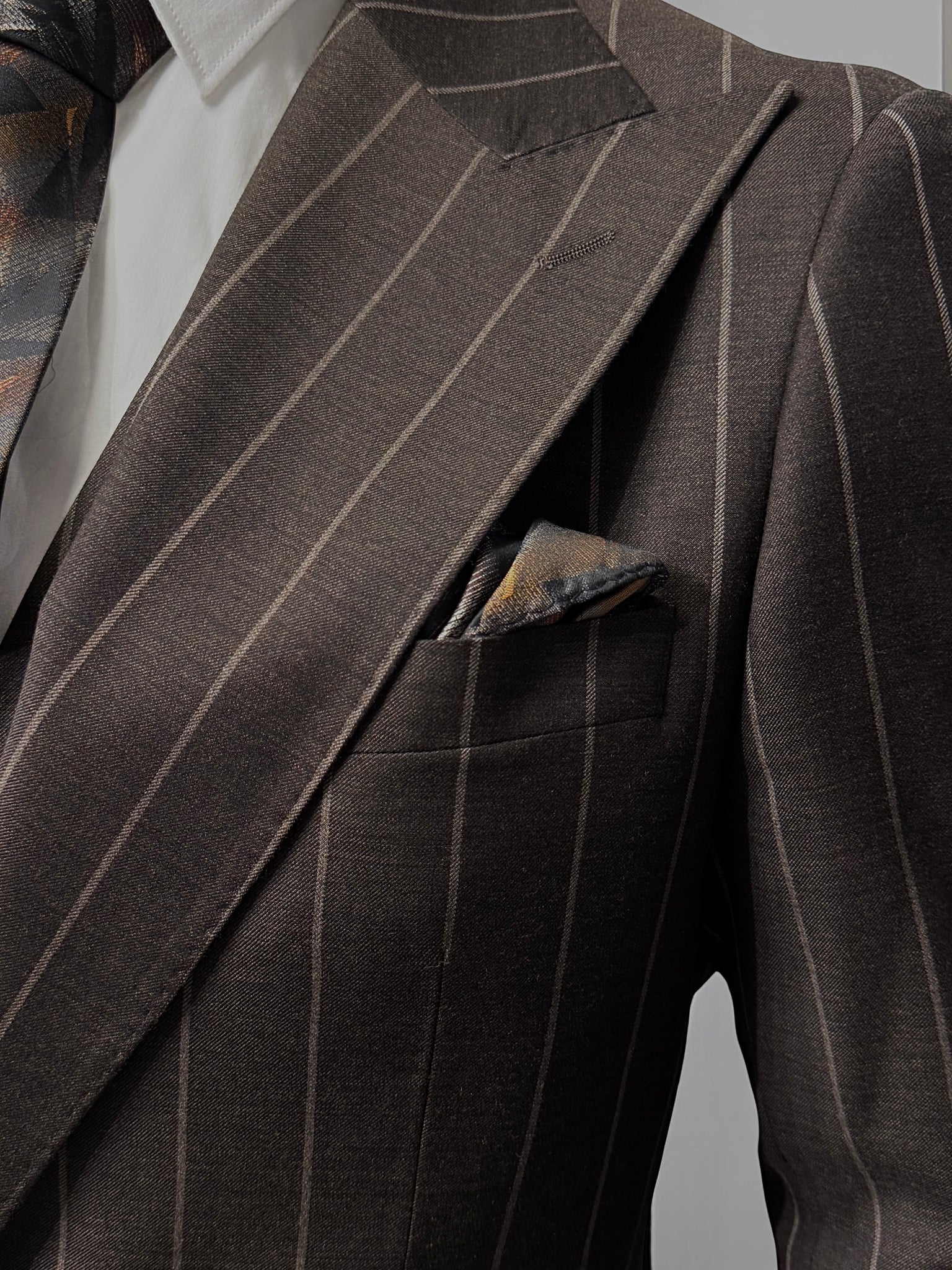 A mannequin displays the Tiglio Rosso Orvietto Brown Pinstripe TL8101 suit with a white shirt and patterned tie, highlighting the classic style of Tiglio Rosso against a simple light background.