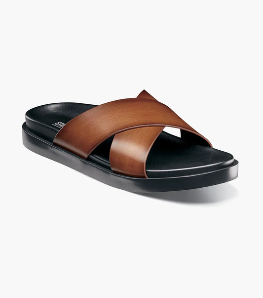 The Stacy Adams Montel Cross Strap Slide Sandal in Cognac (25469-221) features brown leather straps and a black cushioned footbed, perfect for summer. Shown on a white background.