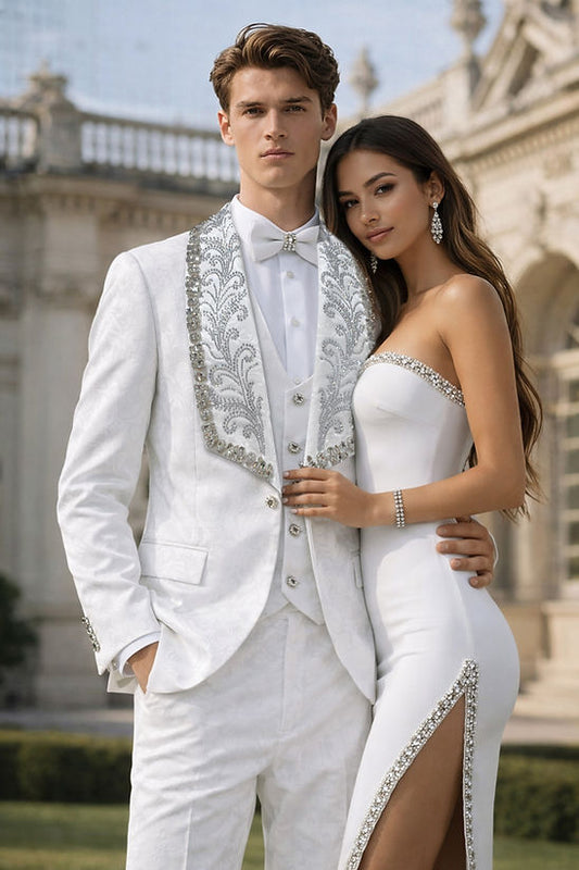 A man wears the MANZINI ASPEN 3-Piece Slim-Fit Men's Fancy Rhinestone Woven Pattern Tuxedo in White/Black by Manzini, standing outdoors beside a woman in a strapless white dress, both posing before a classical building.