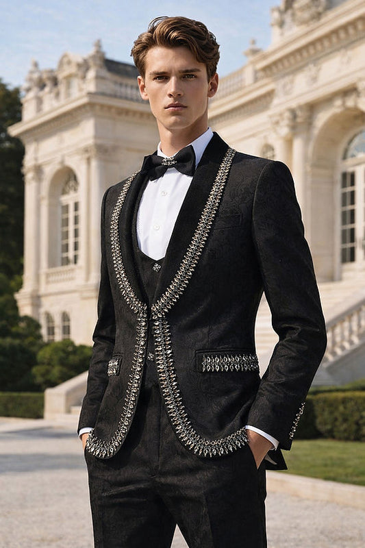 A man in a Manzini RIO 3-Piece Men's Shiny Black Tuxedo Suit with large rhinestone trim and floral pattern stands outdoors before an ornate, classical building.