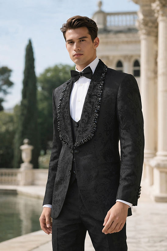 A man wears the MANZINI ASPEN 3-Piece Slim-Fit Men's Fancy Rhinestone Woven Pattern Tuxedo in black by Manzini, with a white shirt and black bow tie, standing outdoors near a classical building and reflecting pool, ready for a formal event.