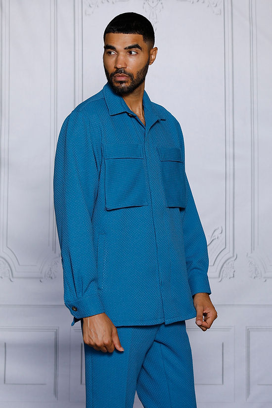 A man wearing the Insomnia INSOMNIA ROBERTO 2PC Teal Leisure Suit stands in front of an ornate white wall.