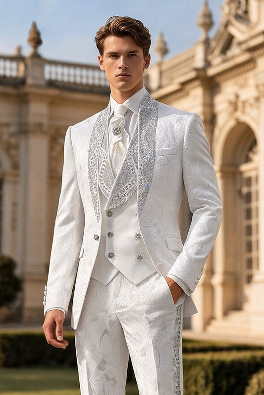 A man wears the Manzini Tower 3-Piece Slim-Fit Vintage Tuxedo Prom Wedding Suit with rhinestones in white, featuring a shawl lapel, standing outdoors before an ornate classical building.