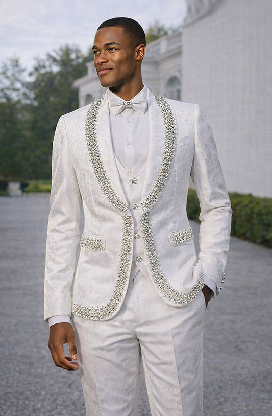 A man wears the MANZINI RIO 3-Piece Men's Shiny Floral Tuxedo Suit in white by Manzini, featuring a floral pattern, large rhinestone trim, satin shawl lapel, white shirt, and bow tie—perfect for prom.