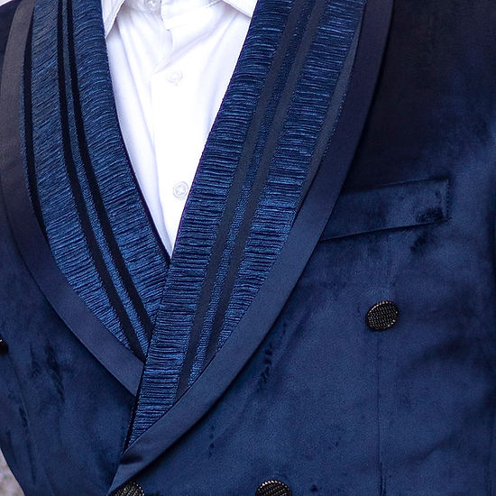 A man with dark hair and a beard confidently stands against a textured white wall, highlighting his tailored fit in an Insomnia INSOMNIA MZV-562 Tailored Fit Blue Fancy Velvet Sport Coat paired with jeans.