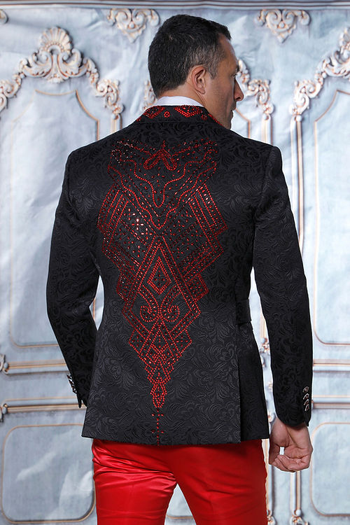 A man in a MANZINI MZS-603 shiny rhinestone floral pattern black/red jacket with red embellishments, paired with red pants, stands before an ornate backdrop.
