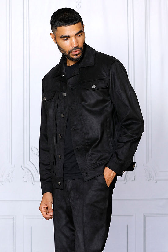 A man with short hair and a beard stands facing forward, wearing the Insomnia INSOMNIA ROMEO 2PC Black Vegan Suede Leisure Suit, set against a light-colored ornate wall.