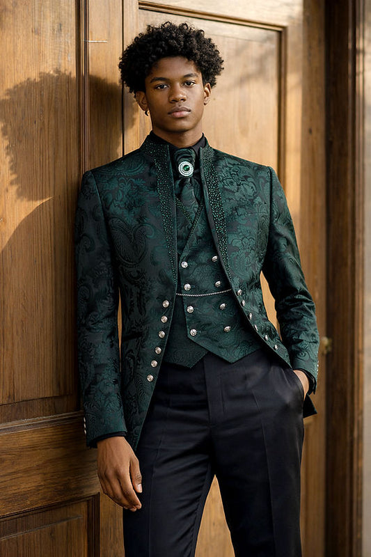 A man stands near a wooden door wearing a Manzini MANZINI LANZINI 3-Piece Slim-Fit Baroque Gothic Tuxedo Prom Wedding Suit w/ Rhinestones Hunter, featuring a dark green floral pattern, matching vest, black pants, rhinestone trim, and brooch.