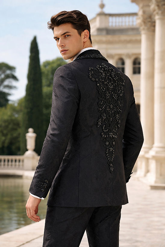 A man wears the MANZINI ASPEN 3-Piece Slim-Fit Men's Fancy Rhinestone Woven Pattern Tuxedo in black by Manzini, with a white shirt and black bow tie, standing outdoors near a classical building and reflecting pool, ready for a formal event.
