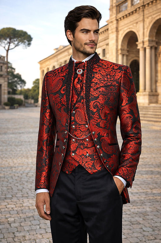A man in a Manzini MANZINI LANZINI 3-piece slim-fit Baroque Gothic tuxedo prom wedding suit with rhinestones in red stands outside near a historic stone building, his outfit featuring ornate details and a stylish cravat.