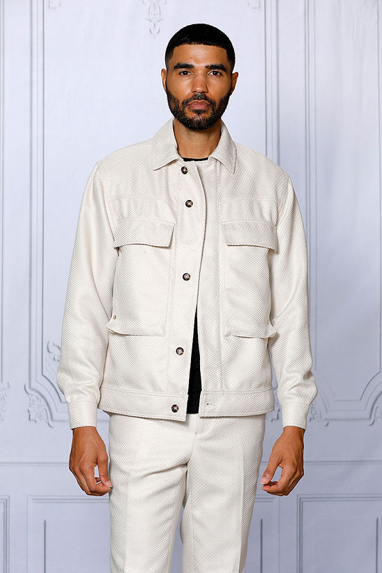 A man with short hair and a beard wears the INSOMNIA FENDI 2PC Tan Leisure Suit by Insomnia, featuring large front pockets, standing against a light-paneled background.