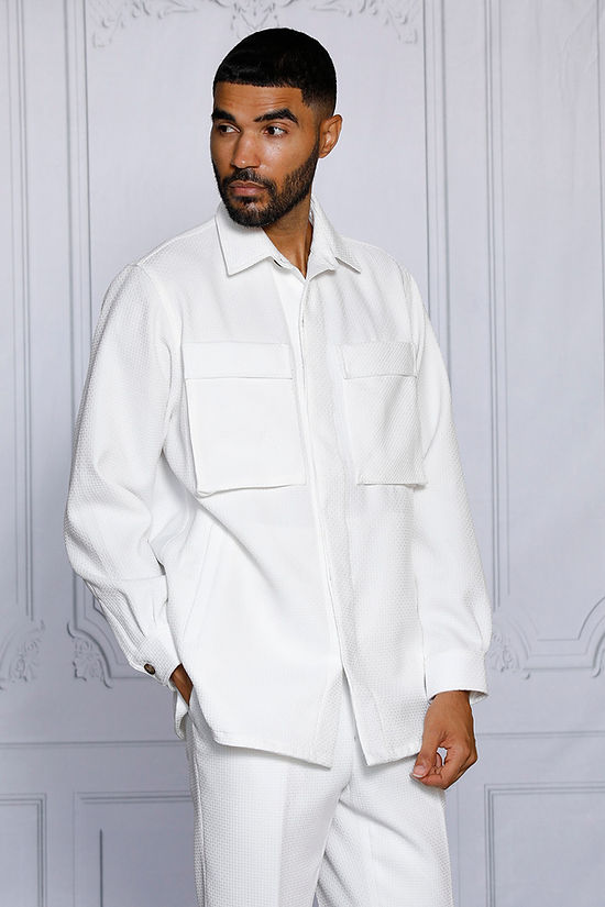 A man with short hair and a beard wears the INSOMNIA ROBERTO 2PC White Leisure Suit by Insomnia, standing against an ornate light-colored wall.