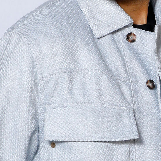 A man wearing the INSOMNIA FENDI 2PC Silver Leisure Suit by Insomnia stands against a decorative light-colored wall, looking to his left.