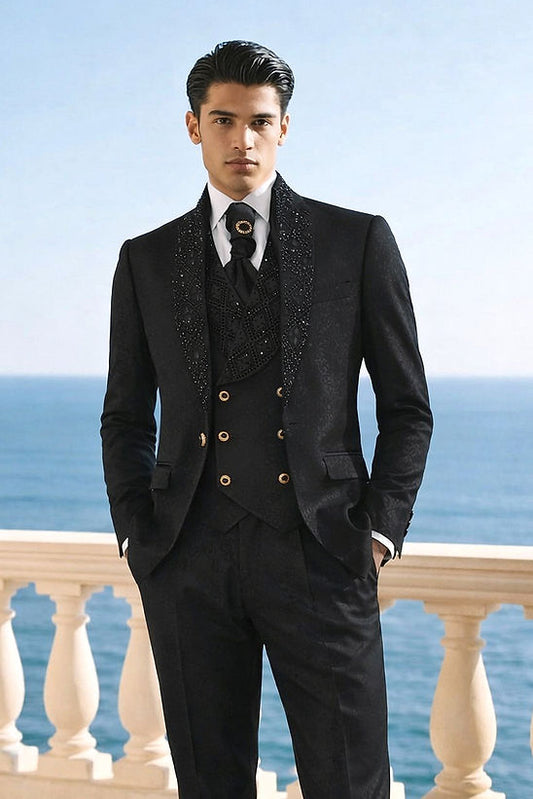 A man in the Manzini HOLLYWOOD 3-Piece Slim-Fit Vintage Black Tuxedo with rhinestones stands outdoors by a stone railing overlooking the sea.