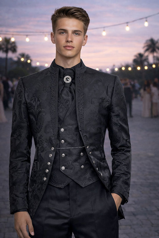 A man wears the Manzini LANZINI 3-Piece Slim-Fit Baroque Gothic Tuxedo Prom Wedding Suit with rhinestones in black, standing outdoors at dusk with string lights and people in the background.