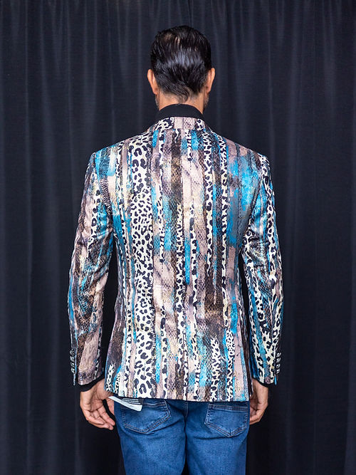 A man wearing a Manzini MANZINI MZS-559 Men's Tailored-Fit Leopard/Reptile Sport Coat Jacket Blazer Blue, a black turtleneck, and blue jeans stands in front of a black curtain.