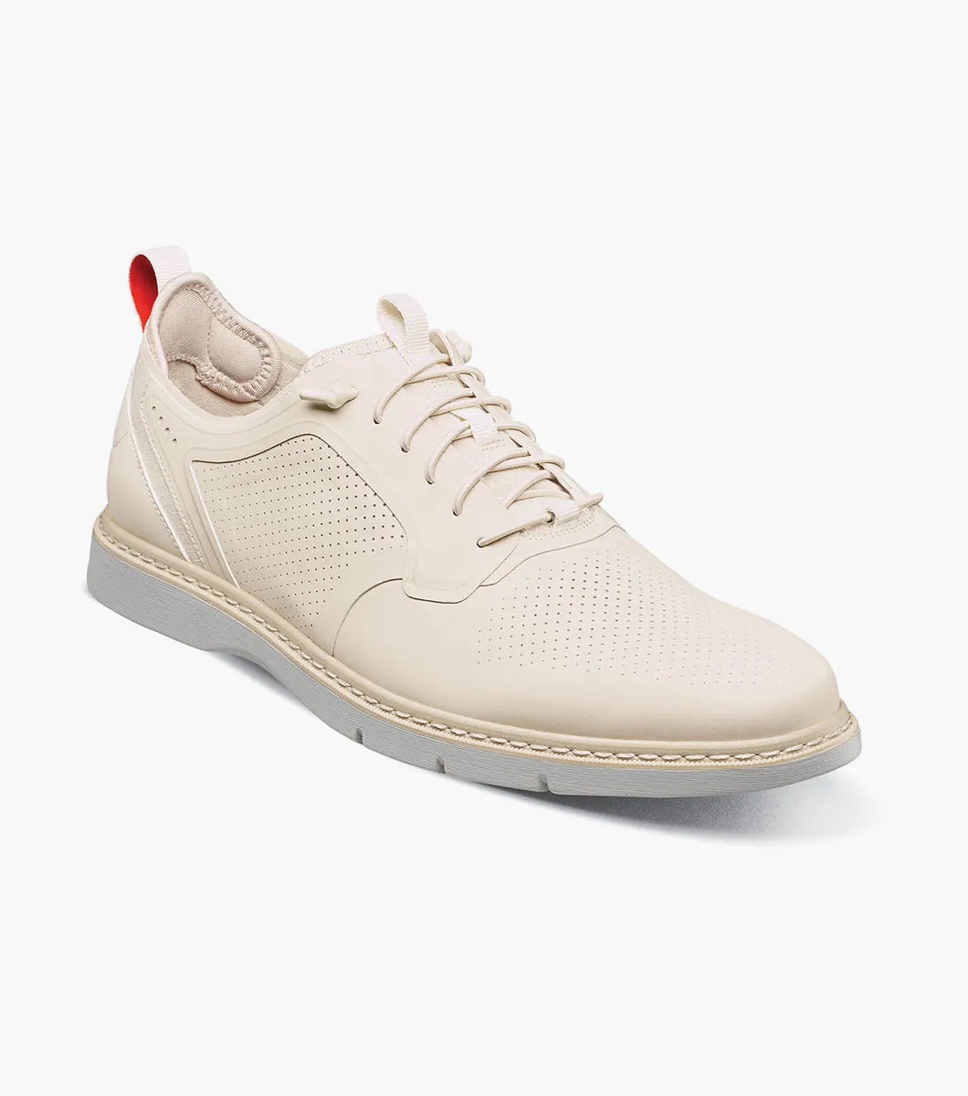 The STACY ADAMS Synchro Plain Toe Elastic Lace Up in cream (25518-113) is a leather dress shoe with perforated detailing, a gray sole, elastic laces, and a red heel pull tab, shown on a white background.