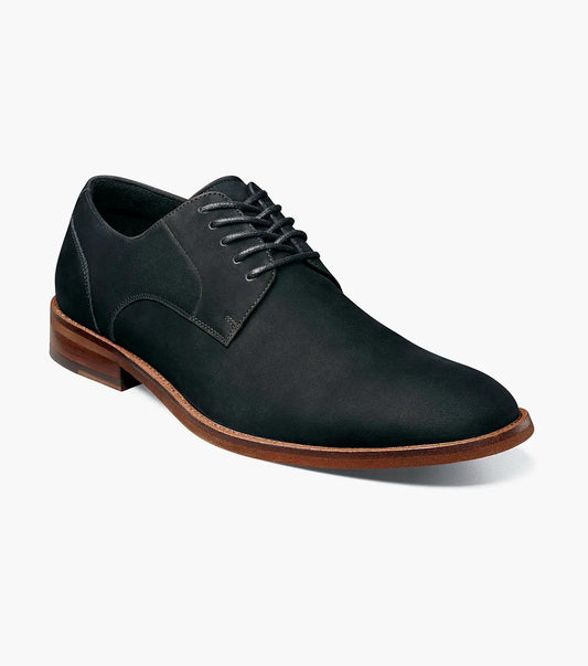 The Stacy Adams Preston Plain Toe Lace Up (25650-001) is a men’s tumbled leather dress shoe in black, featuring black laces, a brown wooden sole, and simple stitching. Displayed elegantly on a white background.