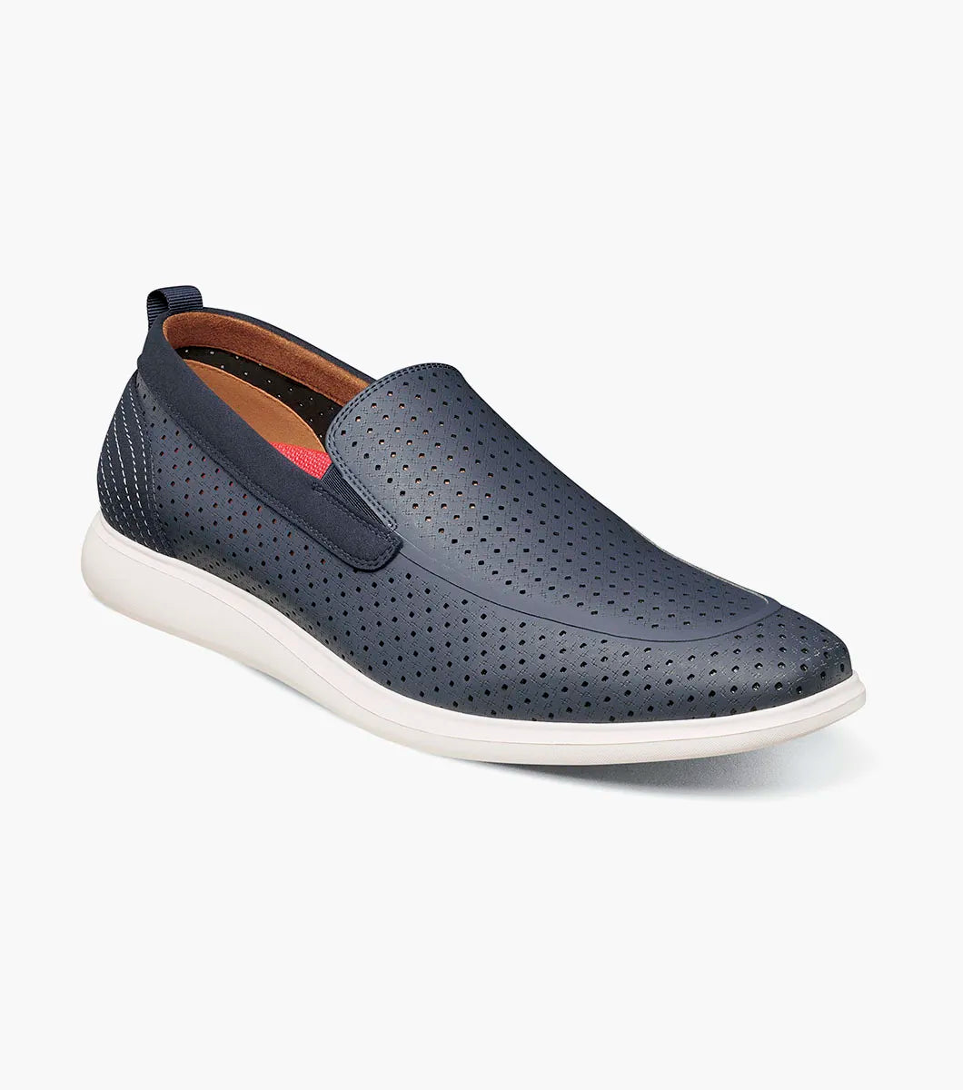 The STACY ADAMS Remy Moc Toe Perf Slip On (Navy, 25658-410) features a navy leather upper with perforated details, white sole, brown lining, and elastic side accents for easy wear, shown against a plain white background.