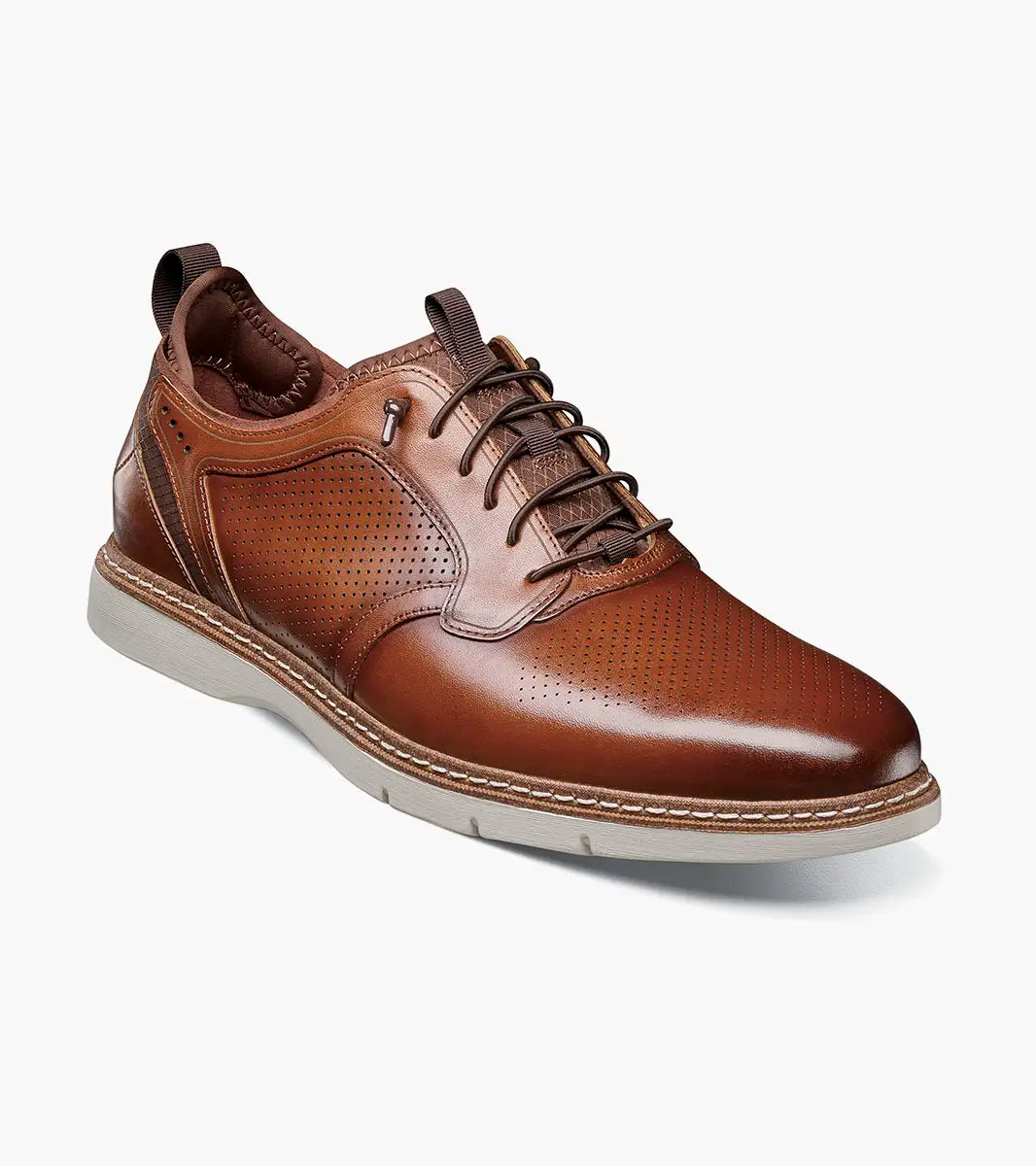 The STACY ADAMS Sync Plain Toe Elastic Lace Up in Cognac (25662-221) is a brown leather men’s sneaker dress shoe with perforated detailing, elastic lace, light gray rubber sole, and RedZone footbed for comfort. Shown on a white background.