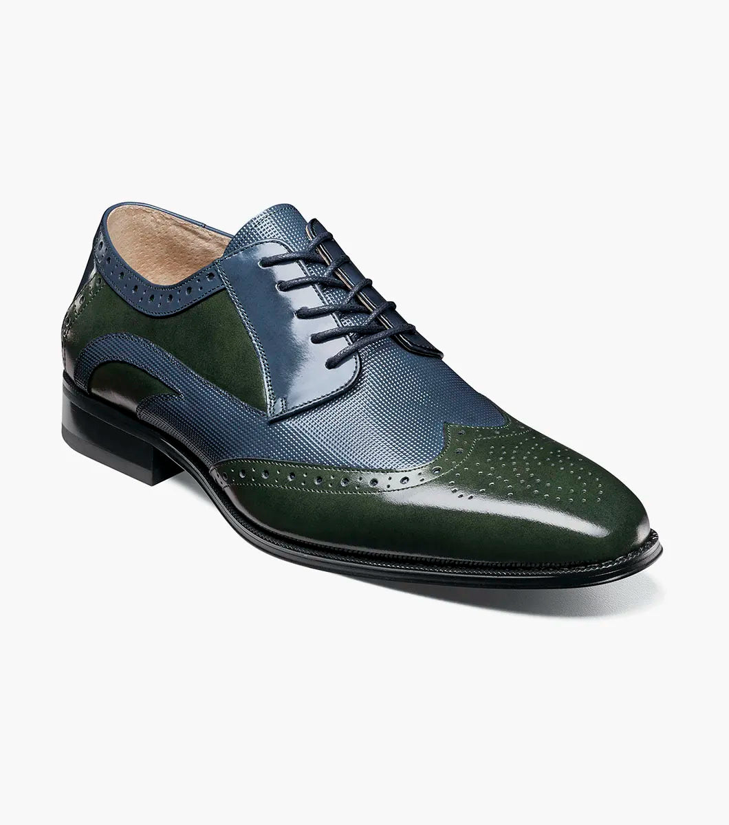 The STACY ADAMS Ivingale Wingtip Oxford (25684-411) is a men's dress shoe in navy and green leather with brogue details, closed lacing, and a black sole, shown on a white background.