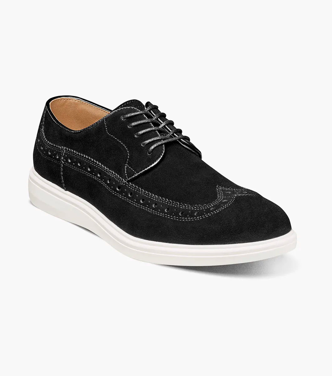 The Stacy Adams Trudell Wingtip Lace Up in black suede features white stitching, a thick white rubber sole, and anatomical arch support for comfort, displayed in a side profile against a plain background.