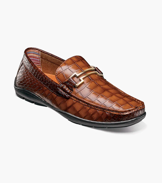 The STACY ADAMS Embrey Moc Toe Bit Slip On in Cognac (25703-221) features brown crocodile print leather, a metallic buckle, a cushioned footbed for comfort, slip-on design, and is showcased against a plain white background.