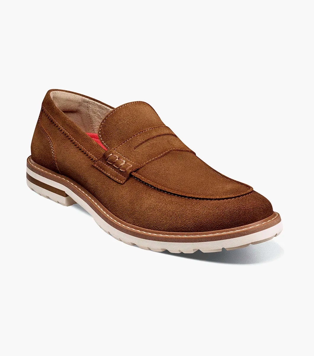 The STACY ADAMS Hopkins Moc Toe Penny Slip On in brown suede (25708-245) features a low heel, visible stitching, white rubber sole, and enhanced arch support, shown on a plain white background.