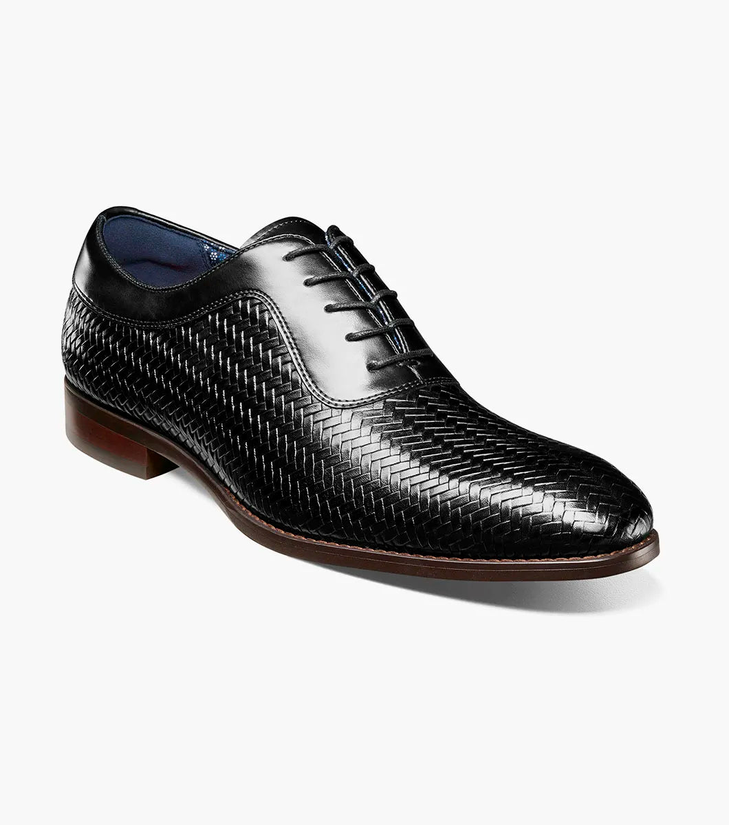 The Stacy Adams Keating Plain Toe Oxford (25709-001) is a black leather dress shoe with a woven pattern, closed lacing, cushioned footbed, and brown sole by STACY ADAMS, shown on a white background.