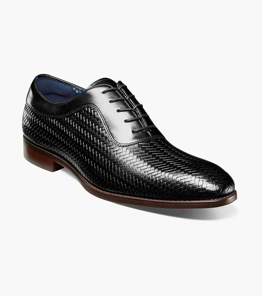 The Stacy Adams Keating Plain Toe Oxford (25709-001) is a black leather dress shoe with a woven pattern, closed lacing, cushioned footbed, and brown sole by STACY ADAMS, shown on a white background.