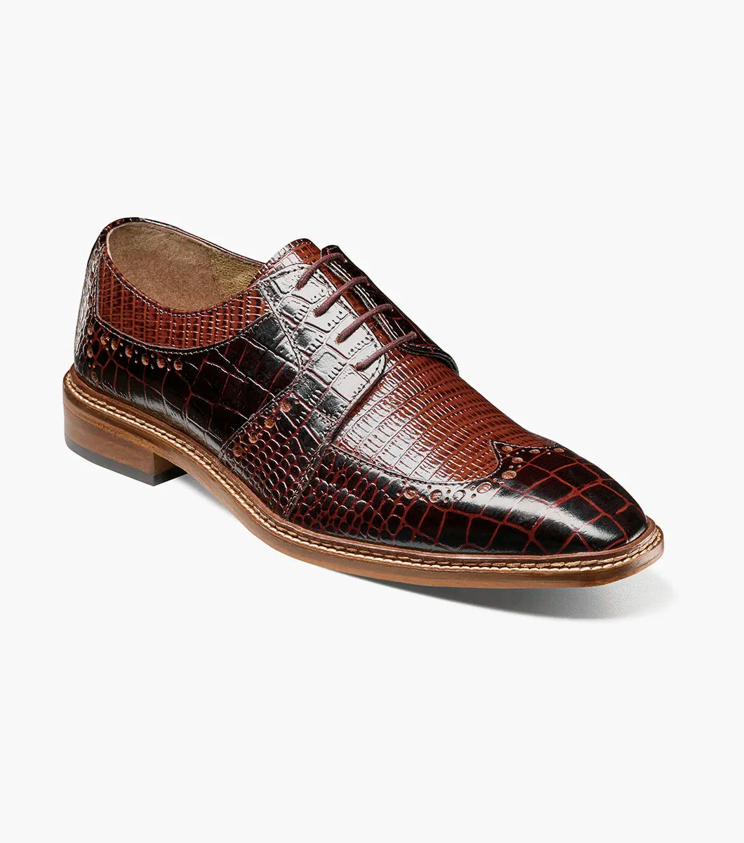 The STACY ADAMS Travato Wingtip Oxford (Brown Multi, 25737-249) features a crocodile-patterned leather upper, laces, and a wooden sole, shown at an angle on a plain white background.