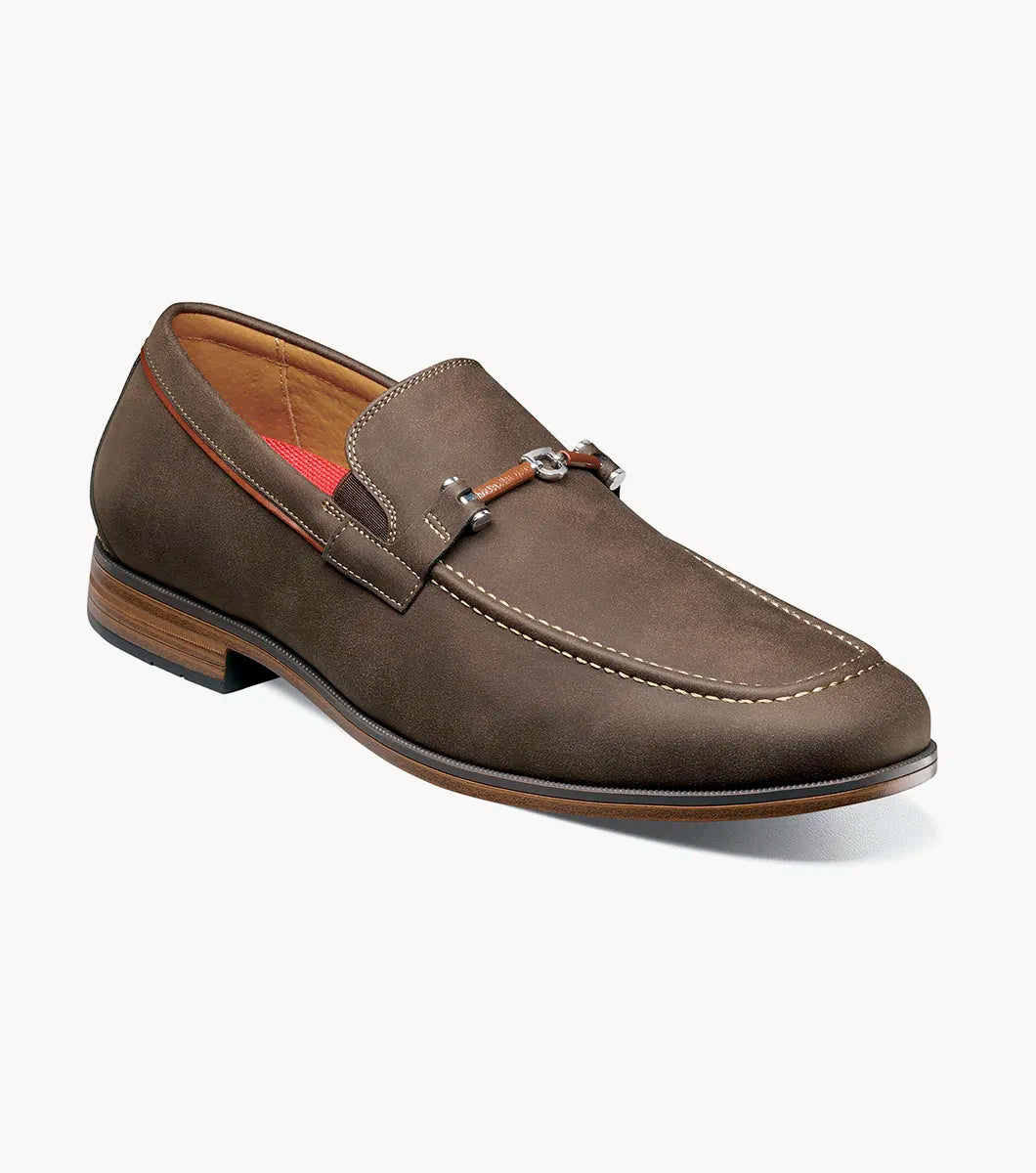 The Stacy Adams Richardson Moc Toe Bit Slip On (Brown, 25746-200) features suede, a metal bit detail, light stitching, red lining, a low wooden heel, and a cushioned RedZone footbed for all-day comfort.