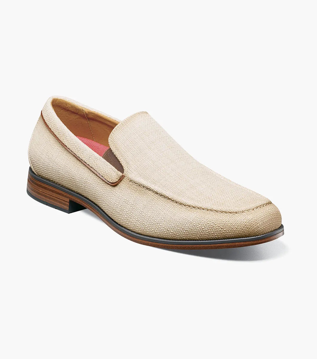 The Stacy Adams Ridgely Moc Toe Slip On (Natural) features a textured fabric upper, brown trim, anatomical arch support, and a low wooden heel for comfort, shown here on a white background.