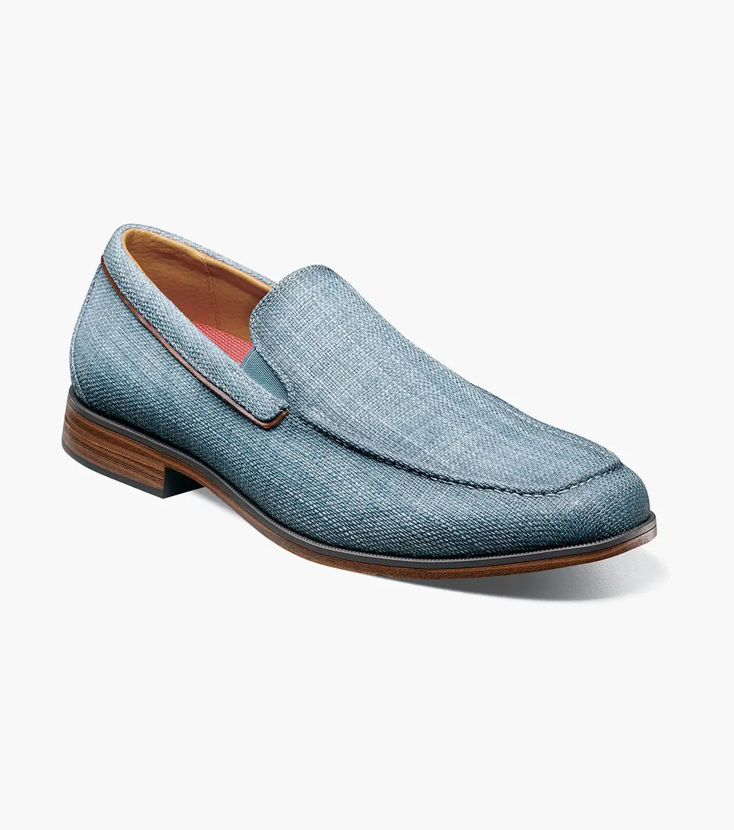 The Stacy Adams Ridgely Moc Toe Slip On in navy features a textured fabric upper, breathable leather lining, brown trim, and a low stacked wooden heel, shown against a white background.