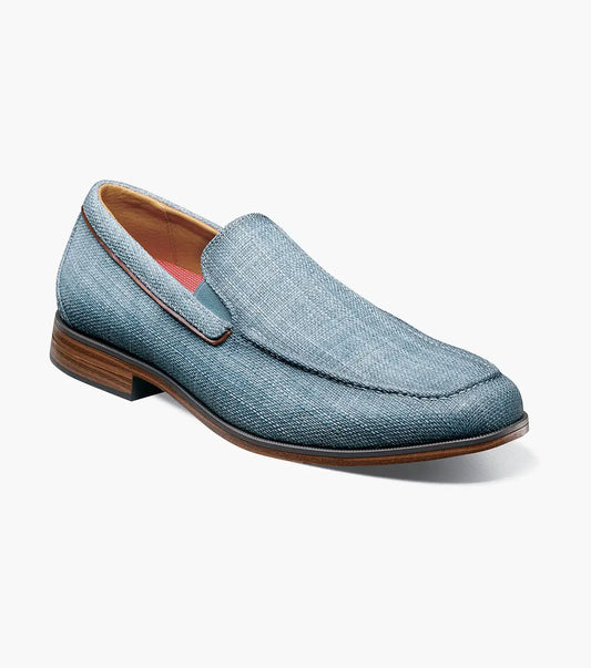 The Stacy Adams Ridgely Moc Toe Slip On in navy features a textured fabric upper, breathable leather lining, brown trim, and a low stacked wooden heel, shown against a white background.