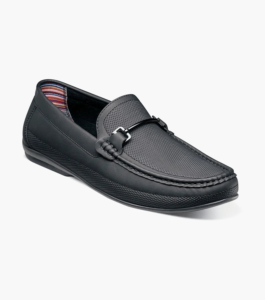 The STACY ADAMS Colton Moc Toe Bit Slip On in black (25760-001) features textured leather, cushioned footbed, metal bit accent, and striped inner lining, shown on a white background.