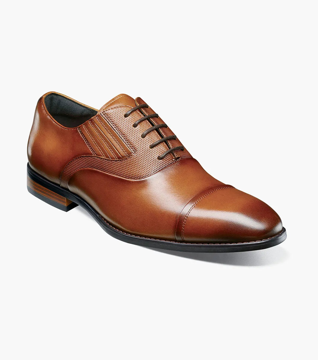 The Stacy Adams Lucas Cap Toe Oxford in Cognac (25766-221) features a brown leather upper with textured side panels, lace-up closure, and low stacked heel for stylish comfort. Men's dress shoe shown on a white background.