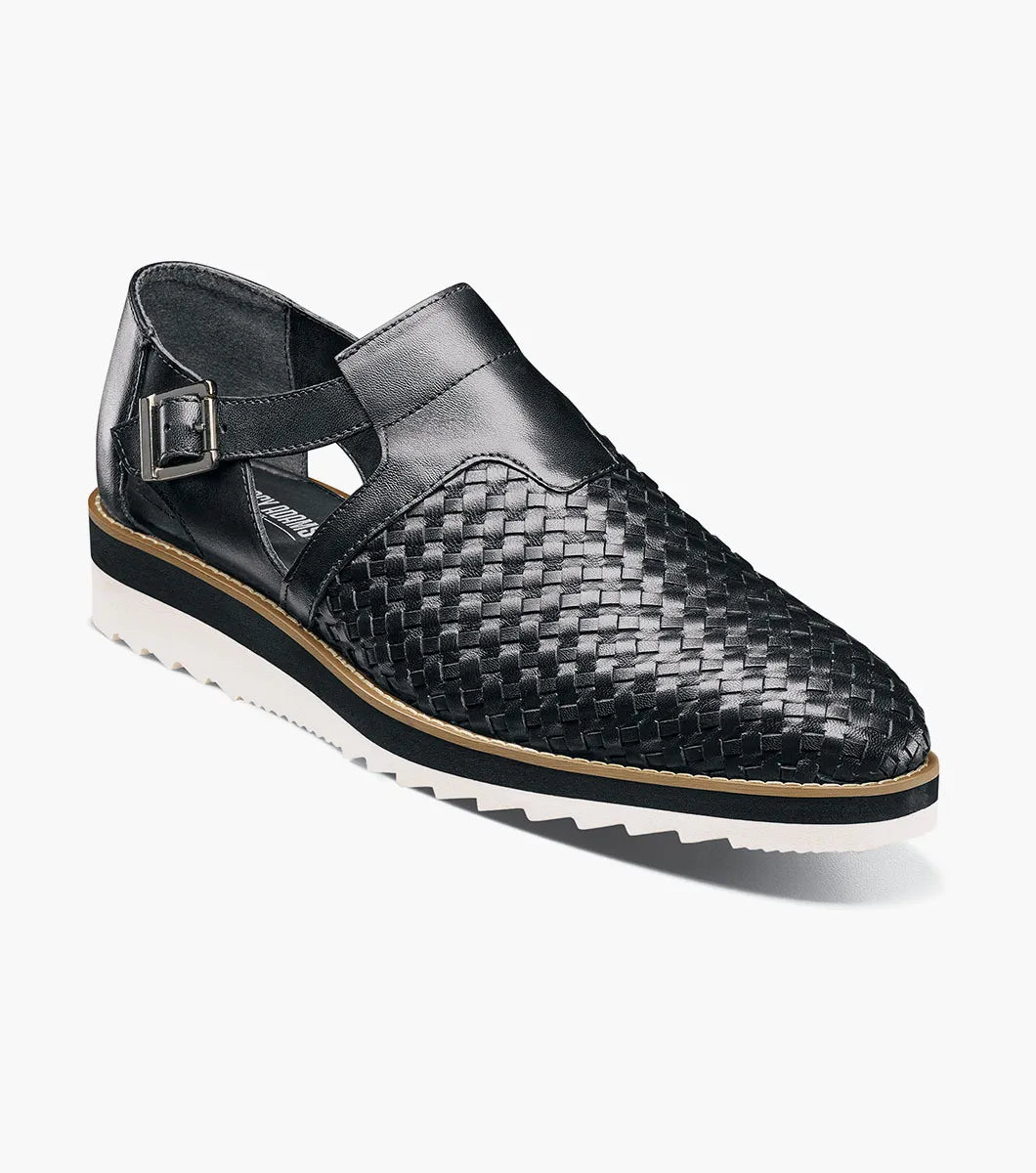 The Stacy Adams Alvarado Woven City Sandal features a black woven leather upper, buckle strap, closed toe, memory foam insole, and a white ridged sole with tan accent.