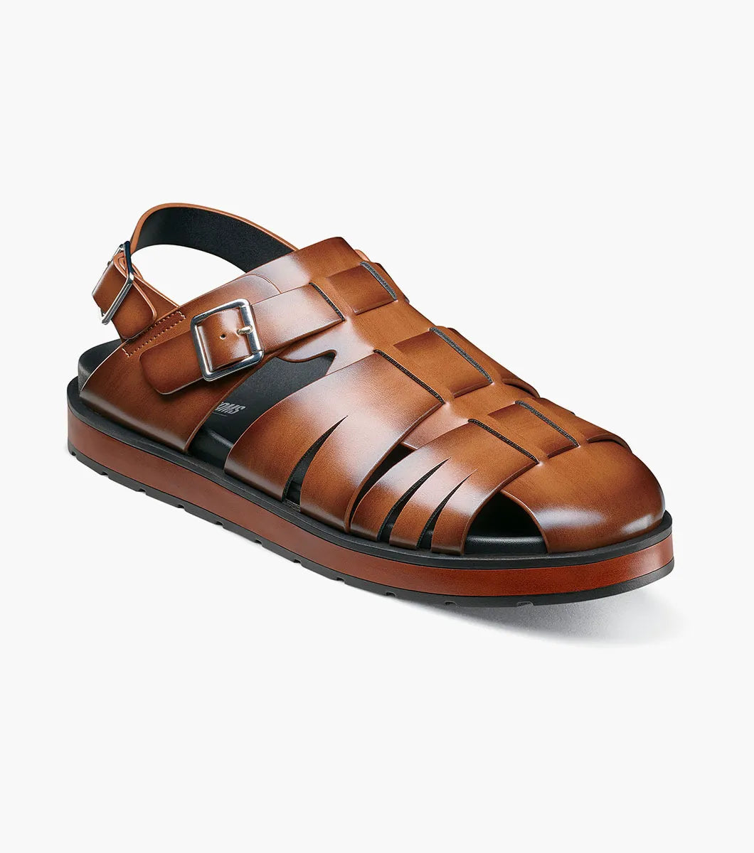 The STACY ADAMS Largo Slingback Buckle Sandal in cognac features a closed toe, woven leather upper, adjustable side buckle, and cushioned black sole—perfect men’s summer footwear. Shown here in style 25773-221 on a white background.