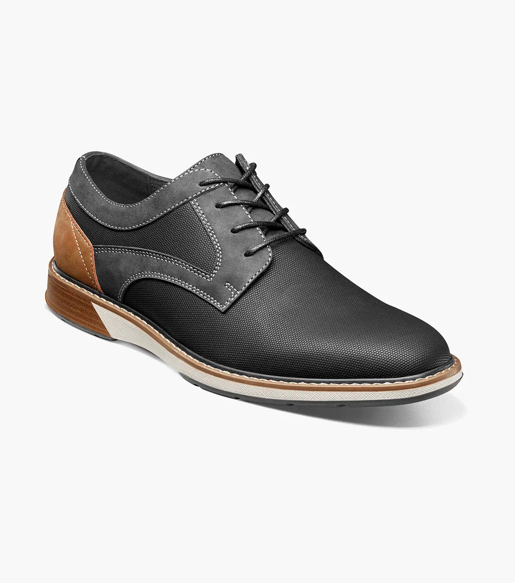 The Stacy Adams Phineas Plain Toe Oxford (25774-001) is a black lace-up oxford with textured material, gray stitching, a brown heel accent, and a cushioned insole for comfort, shown on a white background.