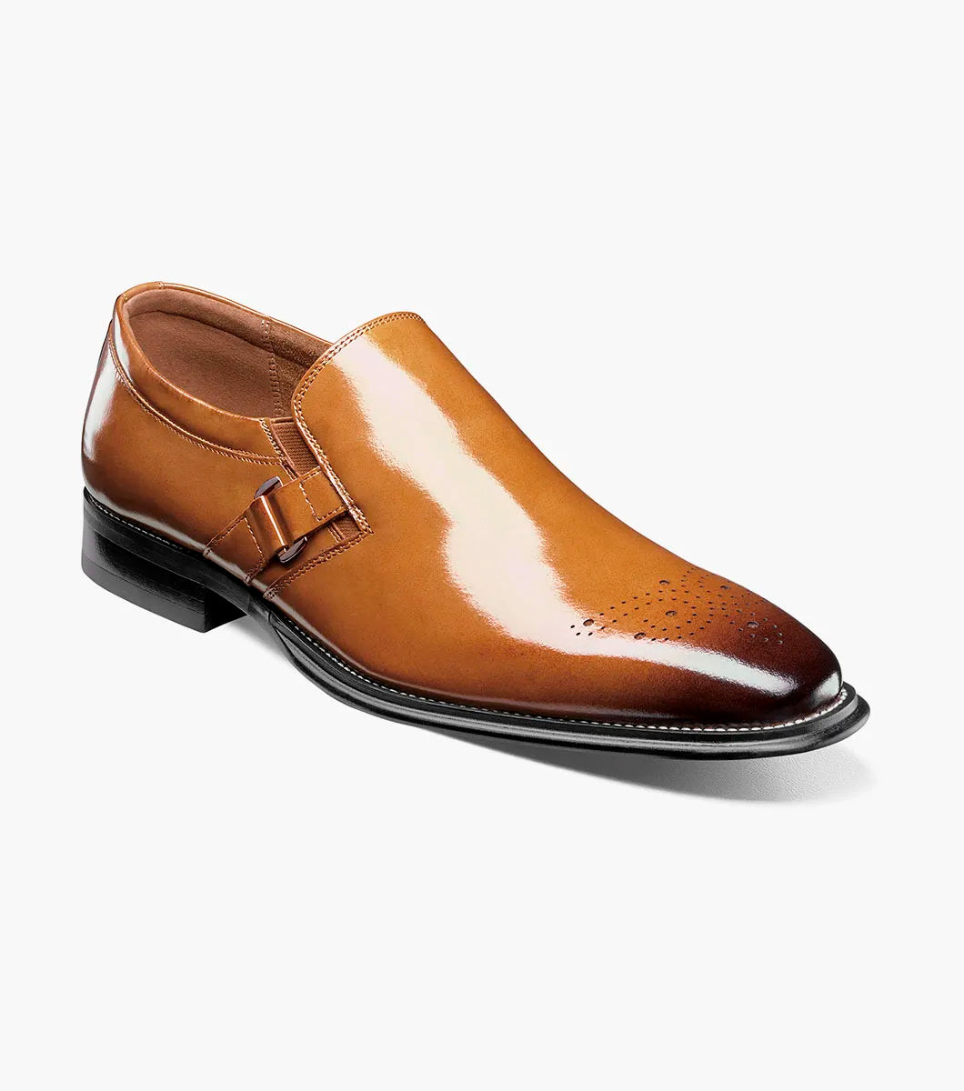 The Stacy Adams Alistair Plain Toe Ornament Slip On (Tan, 25792-240) by STACY ADAMS is a single tan calf leather dress shoe with a pointed toe, decorative perforations, and a side buckle, featuring a comfortable memory foam insole, displayed on a white background.