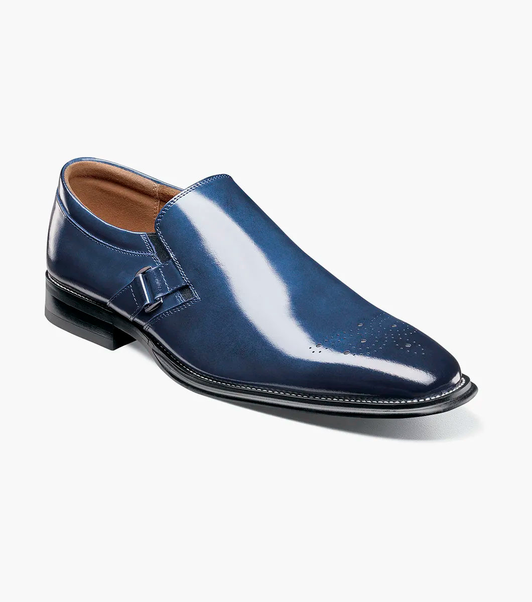 The Stacy Adams Alistair Plain Toe Ornament Slip On in cobalt (style 25792-435) is a single blue calf leather slip-on dress shoe featuring a low heel, decorative perforations on the toe, a side buckle detail, and a comfortable memory foam insole, shown on a white background.