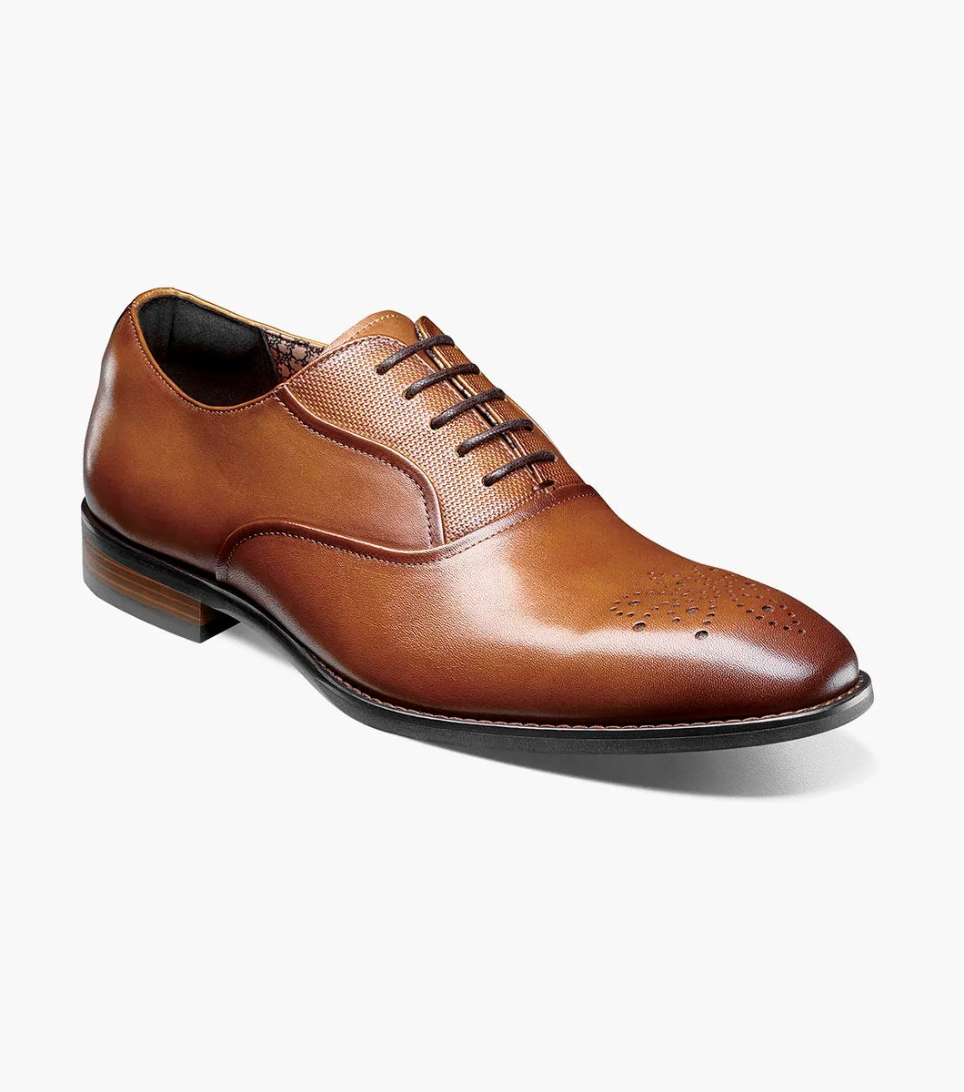 Introducing the STACY ADAMS Langford Plain Toe Oxford in Cognac (25795-221), a men’s dress shoe featuring a rich brown leather upper, subtle decorative perforations on the toe, a low stacked heel, and classic closed lacing. Shown against a white background, these Stacy Adams Oxfords combine timeless sophistication with lasting comfort.