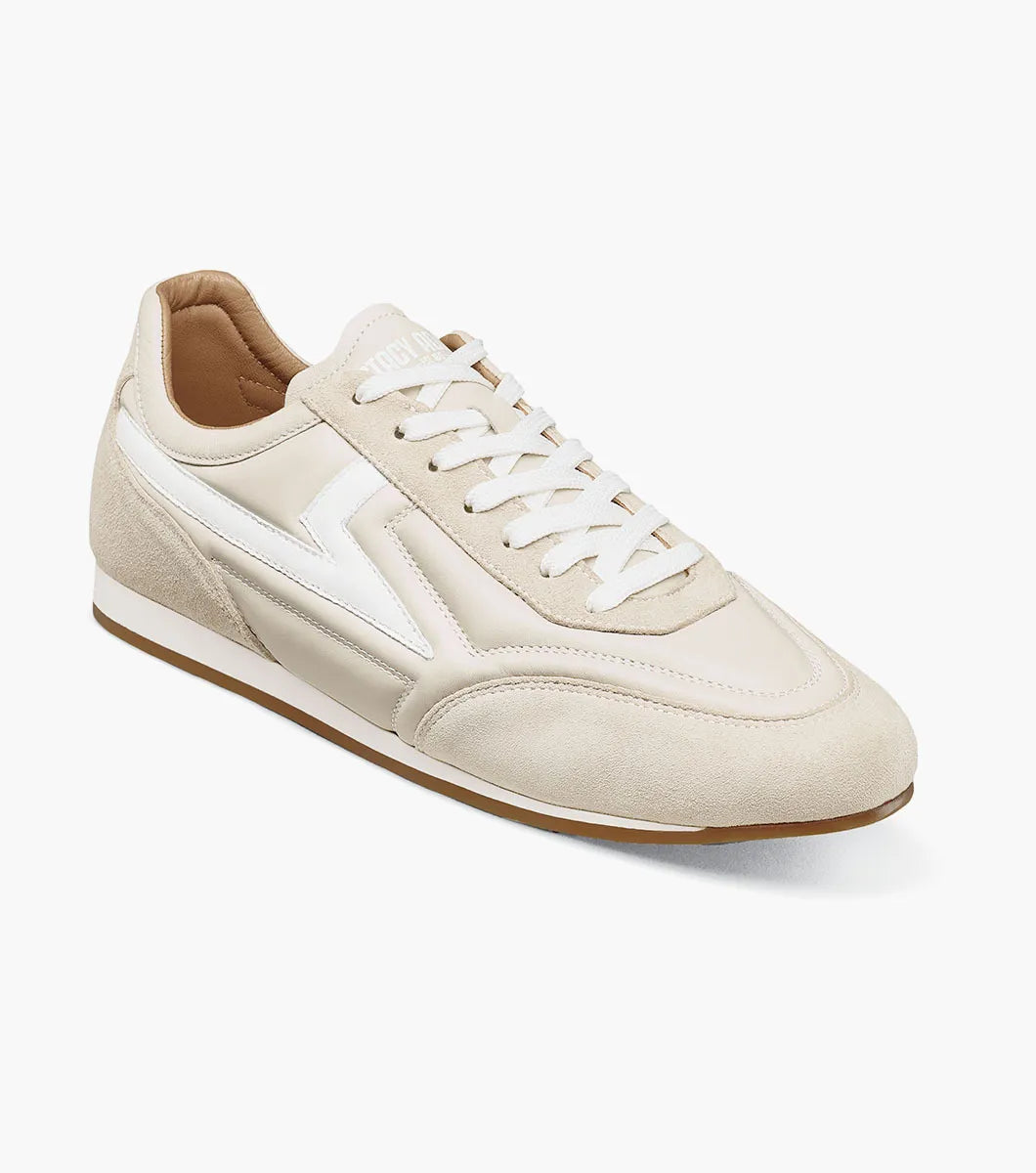 The STACY ADAMS Stacy Adams - Action 150 Sporty Lace Up in Cream (25797-113) is a beige and white low-top modern sneaker with a cushioned footbed, featuring white laces, sleek white side detailing, and a tan rubber sole, photographed on a white background.